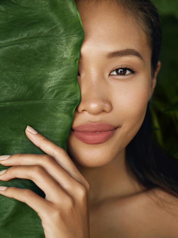 woman hiding half of face behind large green leaf